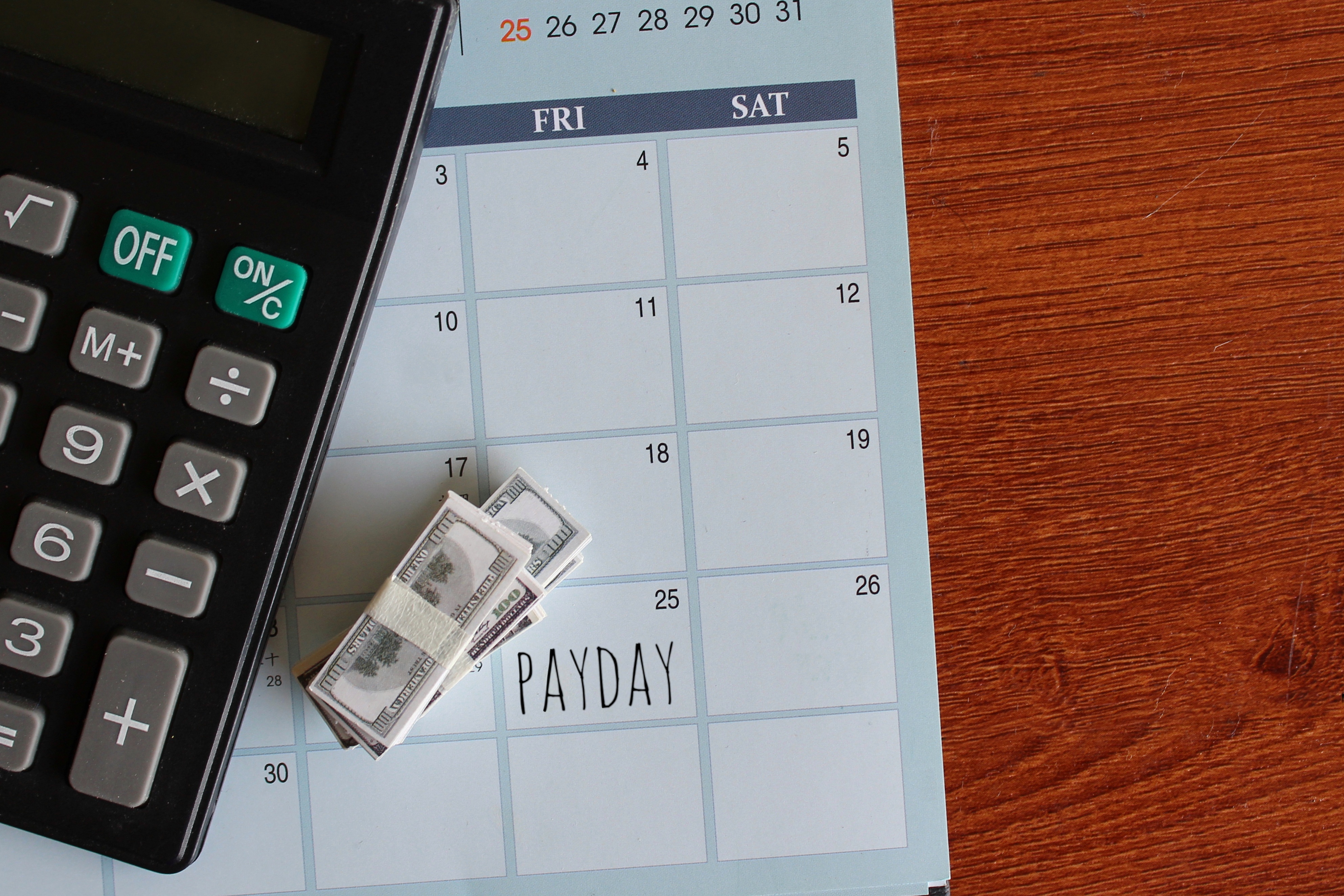 Top view image of banknotes, calculator and PAYDAY written on a calendar